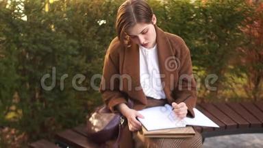 短发女孩坐在公园的长凳上，在一个大笔记本上写一些东西。 准<strong>备考</strong>试的学生